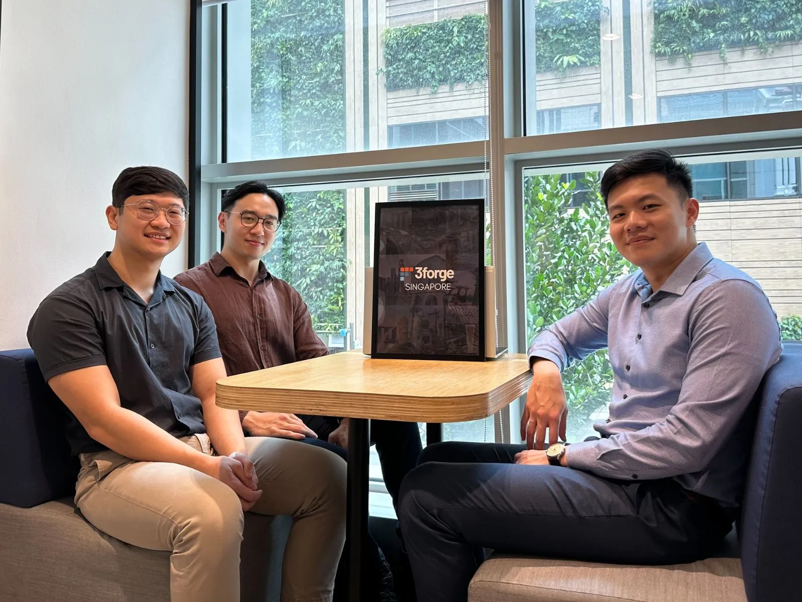 Three digipen singapore alumni sit at a table behind a 3forge logo.