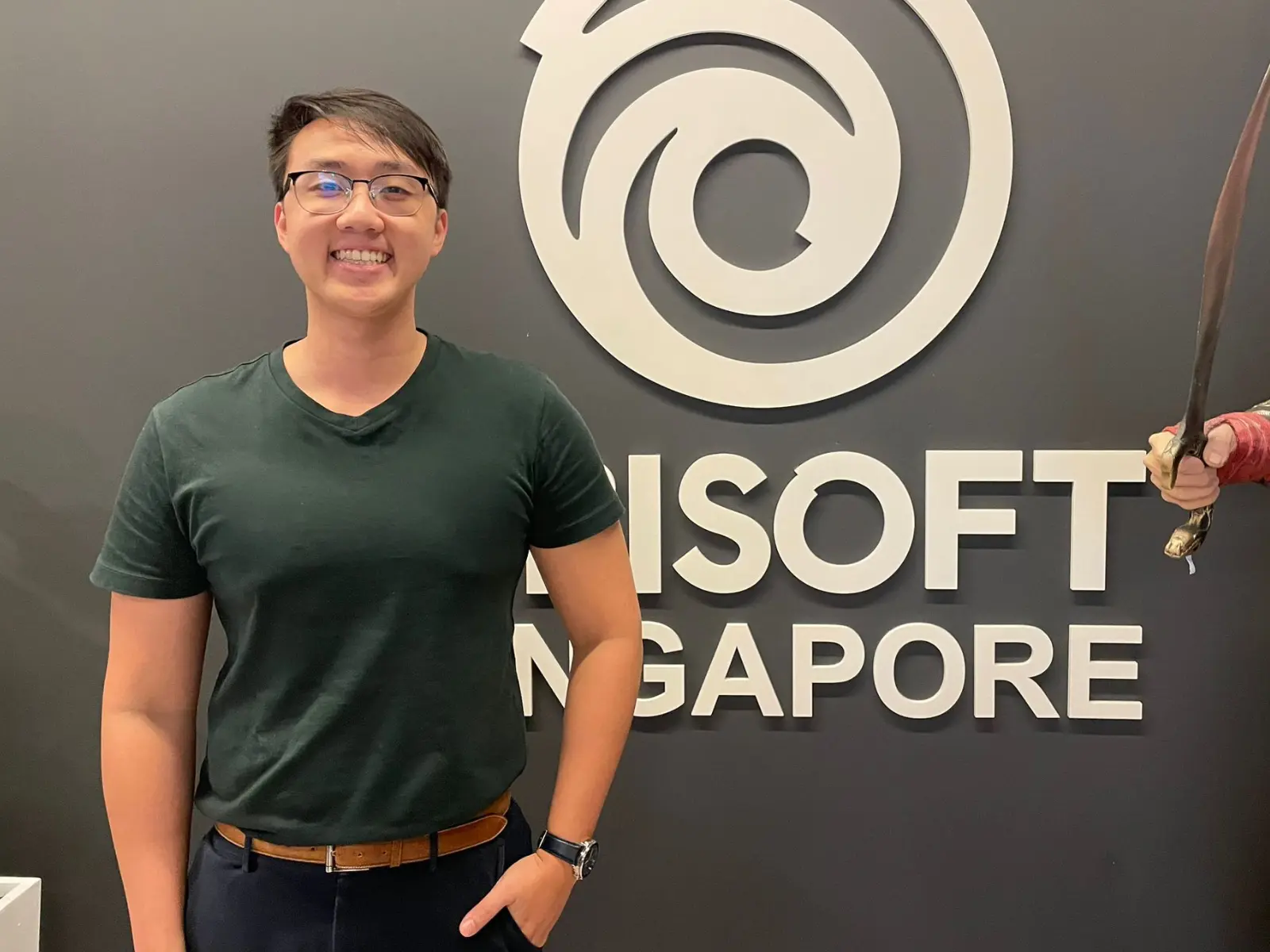 DigiPen Singapore alumni Kenneth Chan stands in front of a Ubisoft Singapore logo.