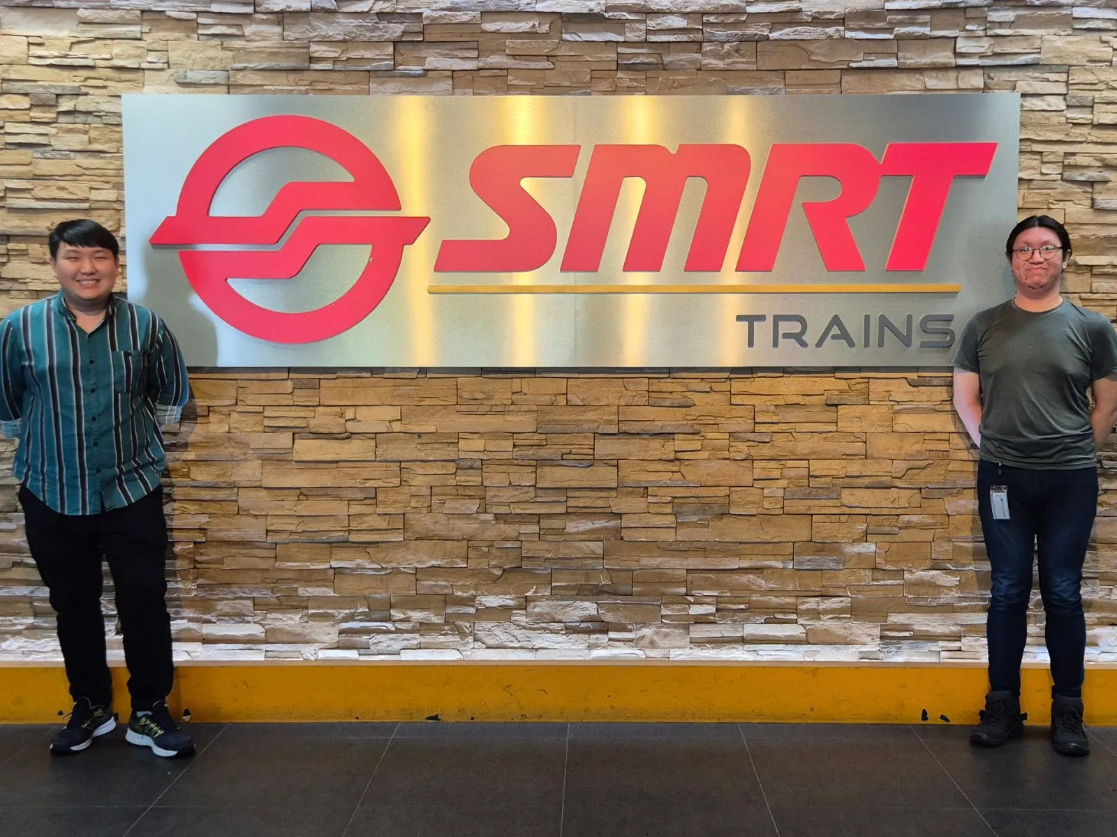 Two DigiPen Singapore graduates stand in front of the SMRT Trains logo.