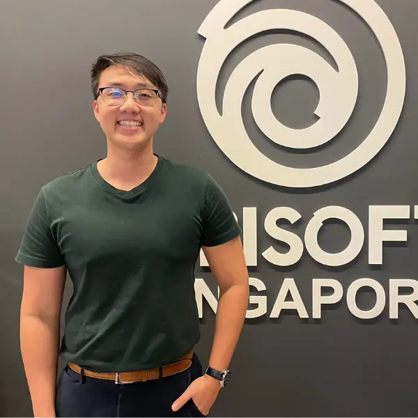 DigiPen Singapore alumni Kenneth Chan stands in front of a Ubisoft Singapore logo.