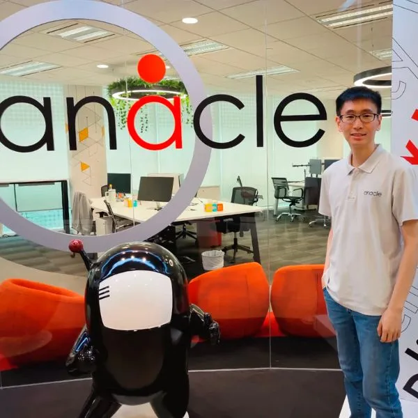 DigiPen graduate, Mok Wen Jie, stands in front of an Anacle Systems logo.